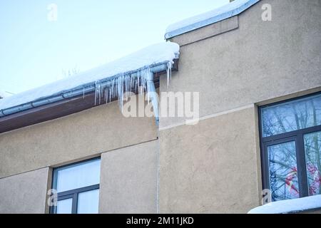 Große Eiszapfen hängen im Winter auf dem Dach des Hauses Stockfoto