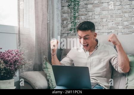 Ein Geschäftsmann, der ein erfolgreiches Marktgeschäft feiert und Geld verdient. Händler, der von zu Hause aus mit einem Notebook Gewinne erzielt. Glücklicher Fanboy, der eine Sportwette gewinnt. Stockfoto