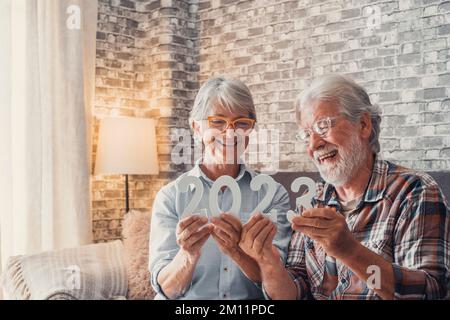 Porträt von zwei alten Rentnern, die zu Hause 2023 zusammenhalten. Nahaufnahme von Neujahrszahlen, Feiern und Zielen für das neue Life-Konzept. Stockfoto