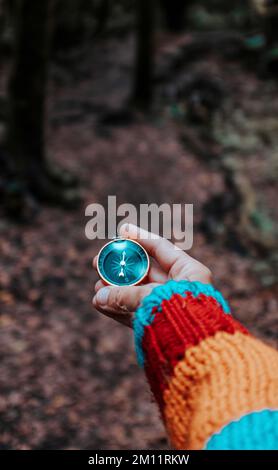 Blickwinkel der Frau, die die Hand hält und einen alten magnetischen Kompass verwendet, um die richtige Richtung und das richtige Ziel zu finden. Konzept sucht nach. Die Menschen genießen Abenteuer im Naturwald Stockfoto