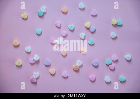 Kleine pastellfarbene Süßigkeiten Herzen mit Sprichwörtern zum Valentinstag, verstreut auf pinkfarbenem Hintergrund, mit Blick auf die Nahaufnahme Stockfoto