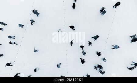 Blick von oben auf die Leute, die im Winter auf einer großen Freiluft-Eislaufbahn Schlittschuhlaufen. Luftfahrt mit Blick auf die Drohne, Flug über die Menge, Skaten auf der Eisbahn. Wintersportaktivitäten. Hintergrund beim Schlittschuhlaufen. City Ice Rink Blau Stockfoto