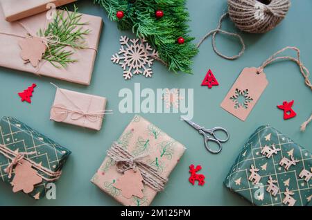 Umweltfreundliche Weihnachtsgestaltung mit Geschenkboxen aus wiederverwendbarem Papier und natürlicher Einrichtung auf blaugrünem Hintergrund, Draufsicht. Umgebung ohne Verschwendung Stockfoto