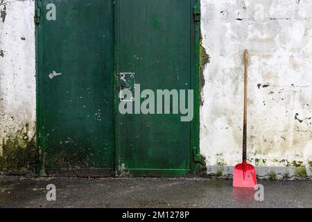 Rote Schaufel an der Wand neben einer grünen Scheunentür Stockfoto