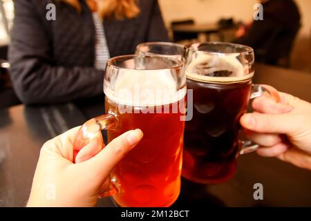 Unschärfe-Tasse mit leichtem Bier. Nahaufnahme von drei Händen, die Bier-steingläser klimpern. Firmenfreunde trinken Bier in einem Pub. Prost. Unscharf Stockfoto