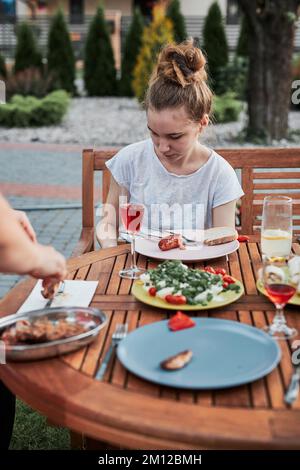 Familie mit einer Mahlzeit vom Grill während des Sommer Picknick im Freien Abendessen in einem Hausgarten. Nahaufnahme von Leuten, die an einem Tisch mit Essen und Geschirr sitzen Stockfoto