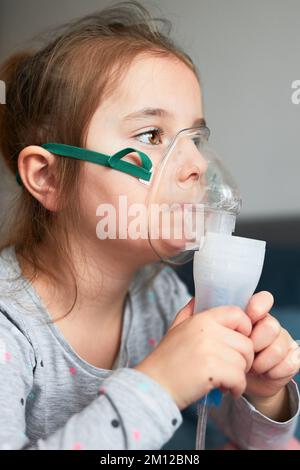 Krankes kleines Mädchen, das eine medizinische Inhalationsbehandlung mit Vernebler hat. Kind mit Atemmaske auf ihrem Gesicht im Bett sitzend Stockfoto