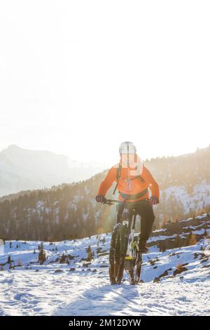 Italien, Venetien, Provinz Belluno, Dolomiten, Radfahrer, die im Winter auf einem modernen E-Bike auf einer Schneereise unterwegs sind Stockfoto