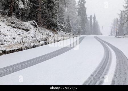 Italien, Venetien, Belluno, Dolomiten. Spuren eines schweren Fahrzeugs im frischen Schnee entlang einer Bergstraße Stockfoto