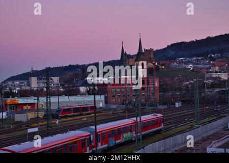 Bingen am Rhein, Deutschland - 10. Januar 2021: Rote Züge auf Gleisen in Bingen am Rhein, Deutschland, mit Kirchen auf Hügeln im Hintergrund sogar im Winter Stockfoto