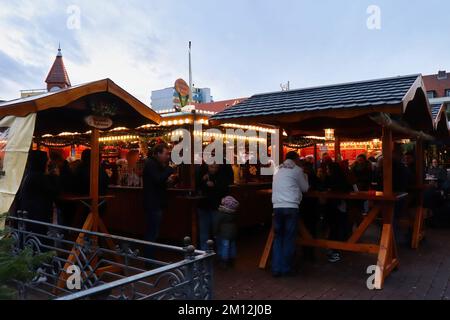 Hanau, Deutschland - 15. Dezember 2019: Menschen, die an Tischen stehen, essen und trinken auf einem Weihnachtsmarkt in Hanau. Stockfoto