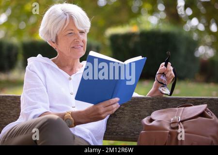 Pensionierte Frau liest ein Buch auf der Bank Stockfoto