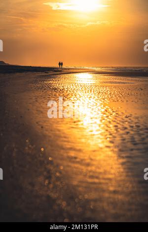 Abendliche Atmosphäre am Nordseestrand bei Ebbe, in der Ferne zwei Menschen als Silhouetten, verschwommener Vordergrund Stockfoto