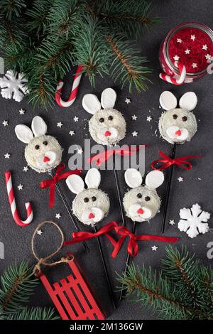 Süße Idee für Weihnachtsgeschenke - Kuchenpops Kaninchen aus Keksen in weißer Schokolade, Kokosflocken und Marshmallows auf grauem Hintergrund, Draufsicht Stockfoto