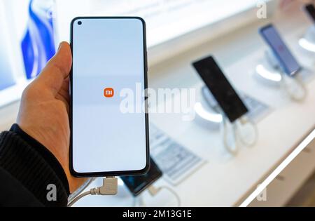 Smartphone mit Xiaomi Logo auf dem Bildschirm in der Hand. Kunde, der sich für ein Smartphone im Geschäft mit Mobiltelefonen entscheidet Stockfoto