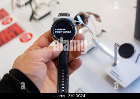 Käufer sieht sich das neue Samsung Galaxy Watch 3-Modell im Elektronikgeschäft an. Samsung Galaxy Watch 3 in der Hand. Gadget, das den Markennamen auf dem Bildschirm anzeigt. Stockfoto