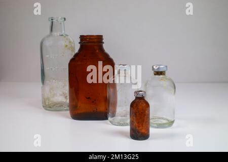 Ein Glas-Reagenzglas, eine Braunglas-Flasche mit medizinischen Pillen, zwei Klarglas-Impfstoffflaschen und eine kleine Braunglas-Impfstoffflasche auf weißem Hintergrund. Stockfoto