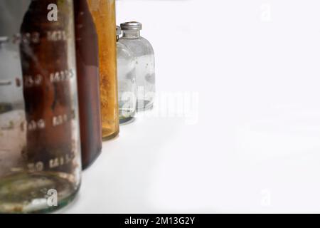 Ein medizinischer Becher, eine medizinische Pillenflasche aus Braunglas, ein Reagenzglas aus Glas und zwei Klarglas-Impfstoffflaschen auf weißem Hintergrund Stockfoto