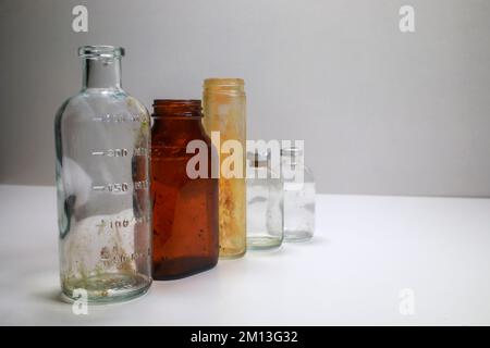 Ein medizinischer Becher, eine medizinische Pillenflasche aus Braunglas, ein Reagenzglas aus Glas und zwei Klarglas-Impfstoffflaschen auf weißem Hintergrund Stockfoto