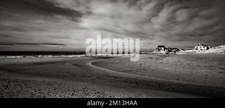 Schwarzweiß-Fotografien des Flusses auf Traeth Llydan Rhosneigr an der Westküste auf der Isle of Anglesey, Nordwales, Vereinigtes Königreich, Herbst. Stockfoto