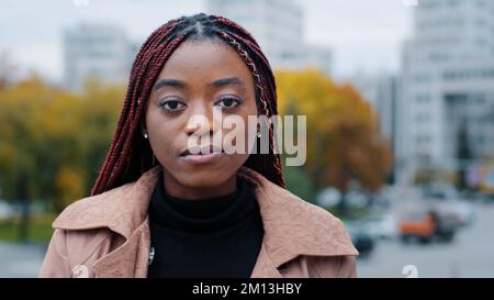 Weibliches Porträt Nahaufnahme junge, ernsthaft pensive, schöne, schicke afroamerikanische Frau, die draußen steht und die Kamera ansieht frustrierte, ethnische Aufregung Stockfoto