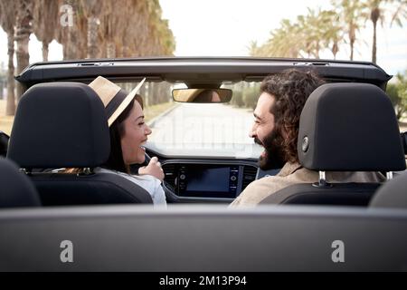 Fröhliches weißes Paar, das an einem sonnigen Tag im Cabrio fährt und sich ansieht und lächelt. Stockfoto