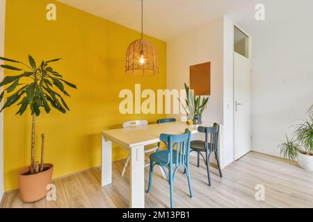 Ein Speisesaal mit gelben Wänden und Holzfußboden, zwei blauen Stühlen und einem weißen Tisch in der Ecke Stockfoto