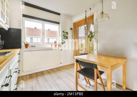 Küche und Essbereich in einem kleinen Haus mit weißen Wänden, Holzfußboden und schwarzen Fliesen an der Wand Stockfoto