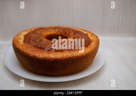 Ein frisch gebackener hausgemachter Rundkuchen mit einem Loch in der Mitte auf einem Gericht, isoliert auf hellem Hintergrund und leerem Platz für Text. Traditioneller Kuchen Stockfoto