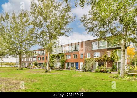 Ein Apartmentkomplex mit Bäumen im Vordergrund und Gras auf dem Boden, umgeben von üppig grünen Rasen unter blauem Himmel Stockfoto