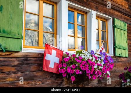 Blumen auf rustikalem Balkon im Frühling mit Schweizer Flagge, Interlaken, Schweiz Stockfoto