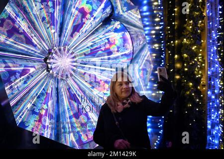 New York, USA. 09.. Dezember 2022. Eine Frau macht ein Selfie vor einem Kaufhaus der Saks Fifth Avenue, Fensterdekoration mit Weihnachtsmotiv, New York, NY, 9. Dezember 2022. Viele große Kaufhäuser dekorieren ihre Fenster in speziell gestalteten Urlaubsthemen, da Weihnachtseinkäufe bis zu 30 % des Jahresumsatzes eines Einzelhändlers ausmachen können. (Foto: Anthony Behar/Sipa USA) Guthaben: SIPA USA/Alamy Live News Stockfoto