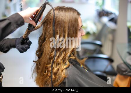 08. Dezember 2022, Sachsen-Anhalt, Wettin-Löbejün: Ein Meisterfriseur bearbeitet einen Kunden mit einem Lockenstab in einem Salon. Die 21-Jährige wird in naher Zukunft den Salon ihrer Großmutter übernehmen. Foto: Jan Woitas/dpa Stockfoto