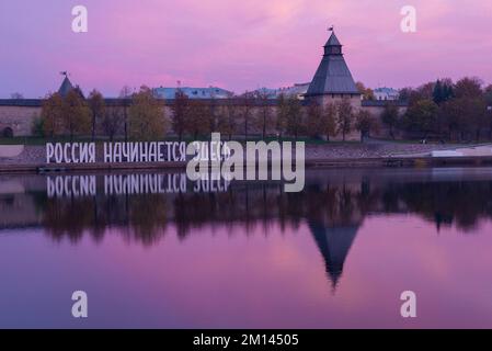 PSKOV, RUSSLAND - 13. OKTOBER 2018: Die Inschrift "Russland beginnt hier" vor dem Hintergrund des Pskow-Kremls in der Oktoberdämmerung. Stockfoto