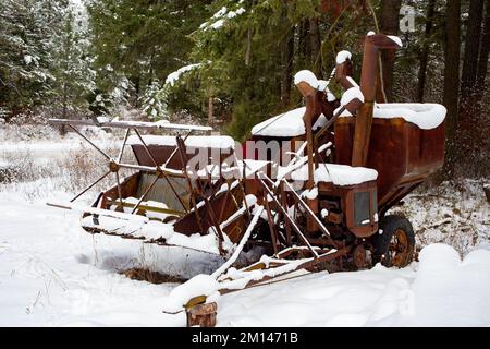 Ein alter, rostiger McCormick-Deering Nr. 63 Harvester Thresher im Schnee, am Waldrand, außerhalb von Bonners Ferry, Idaho. Stockfoto