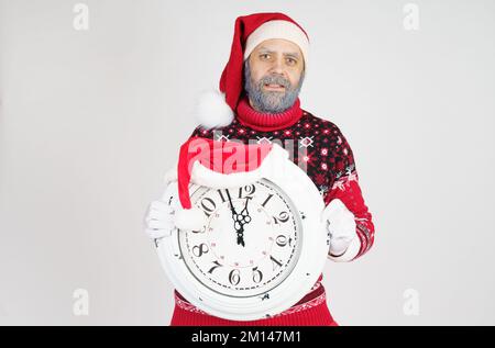 Weihnachts- und Weihnachtskonzept. Der Weihnachtsmann zeigt auf die Uhr vor Weihnachten. Weihnachtsmütze auf der Uhr Stockfoto