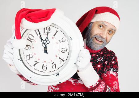Weihnachts- und Weihnachtskonzept. Der Weihnachtsmann zeigt auf die Uhr vor Weihnachten. Weihnachtsmütze auf der Uhr Stockfoto