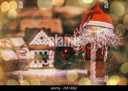 Weihnachtsgeschenk, Lebkuchenhaus, Weihnachtsmann. Wunderschöner Bokeh-Effekt von einer Girlande. Stockfoto