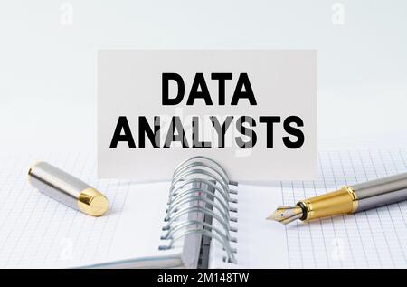 Finanz- und Geschäftskonzept. Auf dem Tisch befinden sich ein Notizbuch, ein Stift und eine Visitenkarte mit der Aufschrift - DATENANALYTIKER Stockfoto