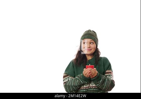 Nachdenkliche hübsche Frau in einem grünen Pullover mit Xmas-Muster, hält eine Kerze in der Hand und lächelt auf mysteriöse Weise auf einen Kopierbereich Stockfoto