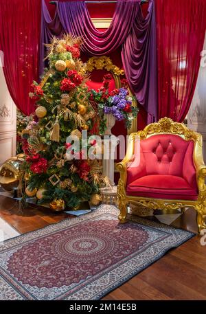 Weihnachtlicher Blick auf den roten Stuhl mit farbenfrohem weihnachtsbaum und Blumen im Hintergrund. Stockfoto