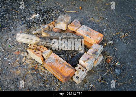 Ein erloschener roter Backsteinherd mit verkohltem Brennholz im Wald aus nächster Nähe. Stockfoto