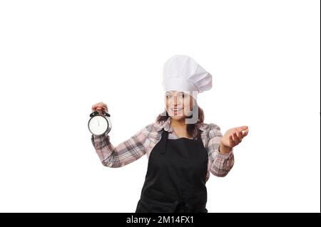 Angenehmer Konditormeister in der Schürze, Wecker, lädt zum Besuch eines neuen Cafés, einer Konditorei oder eines Restaurants zur Eröffnung ein Stockfoto