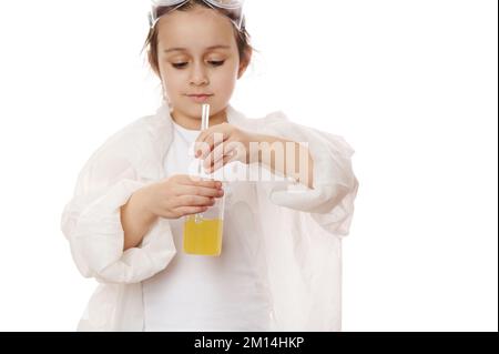 Details: Hände eines Kinderchemikers, der gelbe flüssige chemische Lösung in einem Becher mit Laborstäbchen mischt. Chemie Stockfoto