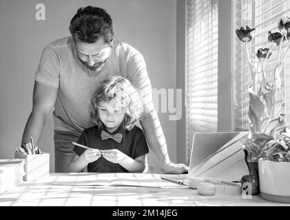 Bärtiger Vater schreibt Schulaufgaben mit seinem Sohn im Klassenzimmer, moderne Bildung Stockfoto