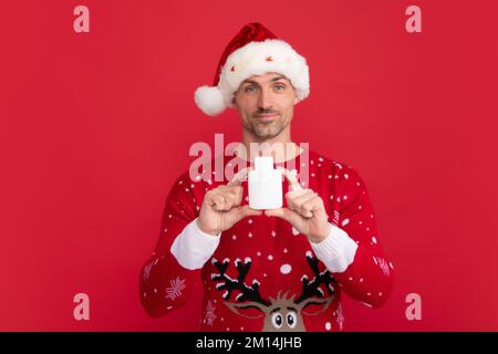 Ein Mann in einem Ferienpullover und Weihnachtsmann hat eine Flasche Medizin im Studio. Stockfoto