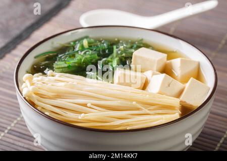 Hausgemachte Miso-Suppe mit Tofu-Käse, Enoki-Pilzen, wachsames Seetang aus nächster Nähe in einer Schüssel auf dem Tisch. Horizontal Stockfoto