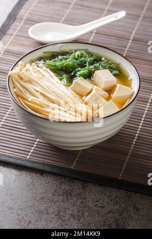 Japanische vegetarische Shiro Miso Suppe mit Tofu, Enoki-Pilzen, wachsames Seetang aus nächster Nähe in einer Schüssel auf dem Tisch. Vertikal Stockfoto