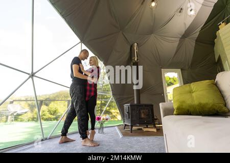 Ein Paar, das die Natur aus Geo-Dome-Zelten betrachtet. Grün, blau, orangefarbener Hintergrund. Gemütlich, Camping, Glamping, Urlaub, Urlaub Lifestyle Konzept. Malerisch Stockfoto