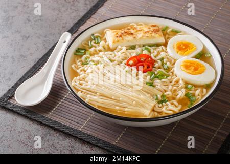 Scharfe Miso-Ramen-Suppe mit Tofu, Enoki-Pilzen, Nudeln, grünen Zwiebeln und Chili in einer Schüssel auf dem Tisch. Horizontal Stockfoto